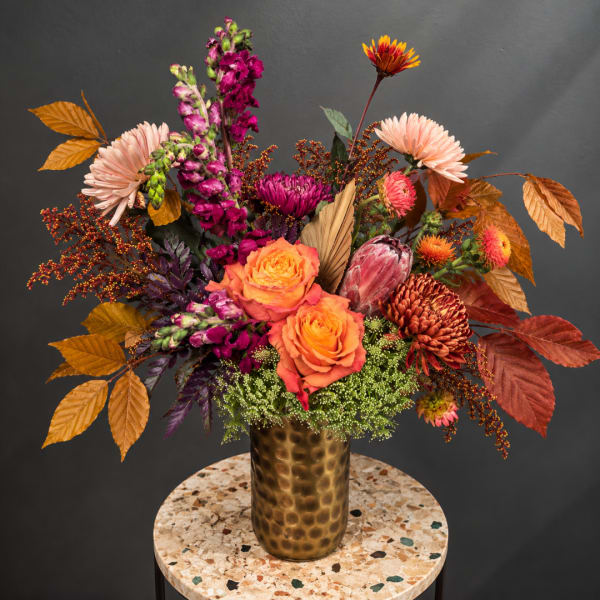 Autumn floral arrangement with roses and chrysanthemums in a gold vase