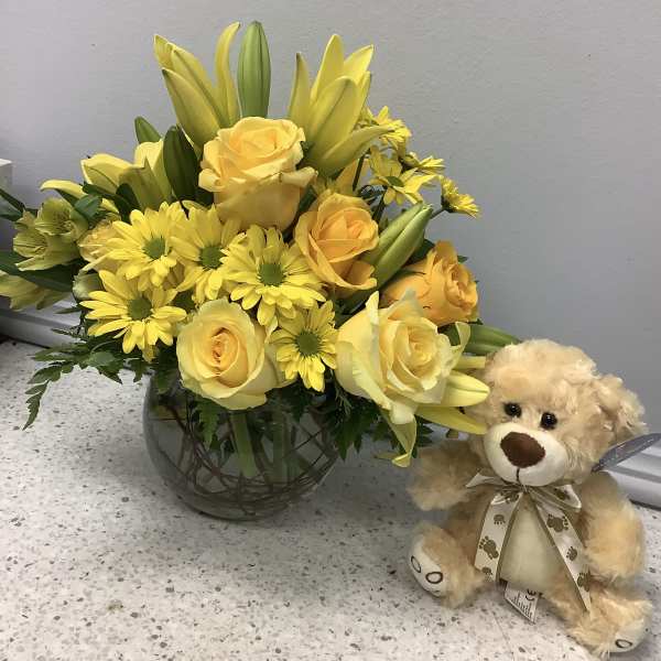 Yellow roses and daisies in a glass vase beside a teddy bear