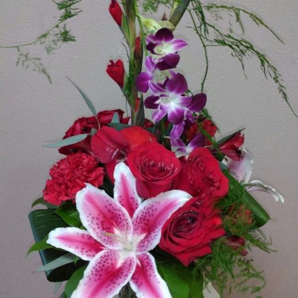 Tall bouquet of red roses, pink lily, and purple orchids in a glass vase