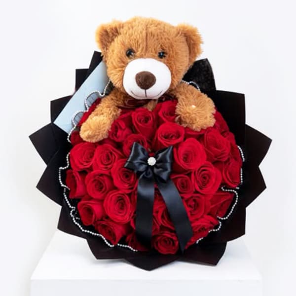 Teddy bear sitting on a bouquet of red roses with a black ribbon