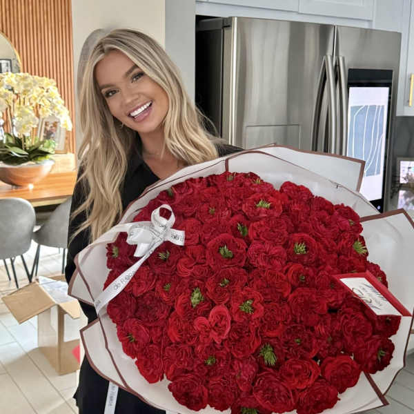 Woman holding a large bouquet of red roses wrapped in white paper