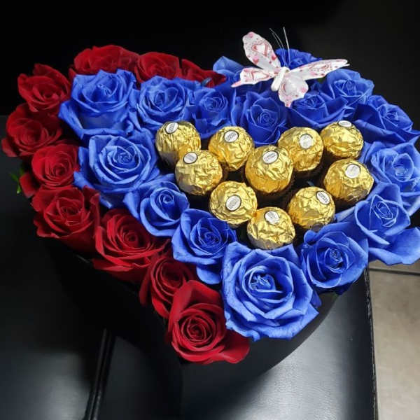 Heart-shaped arrangement of red and blue roses with gold-wrapped chocolates