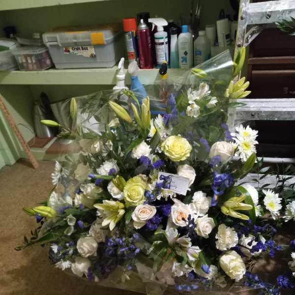 Large bouquet of white, yellow, and blue flowers wrapped in clear plastic
