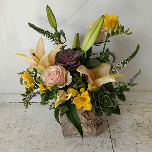 Mixed floral arrangement with lilies, roses, and succulents in a rustic container
