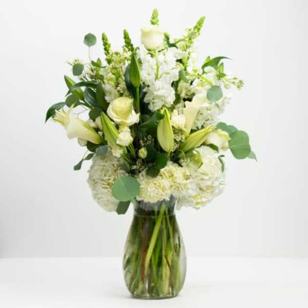 White floral arrangement in a glass vase with green accents