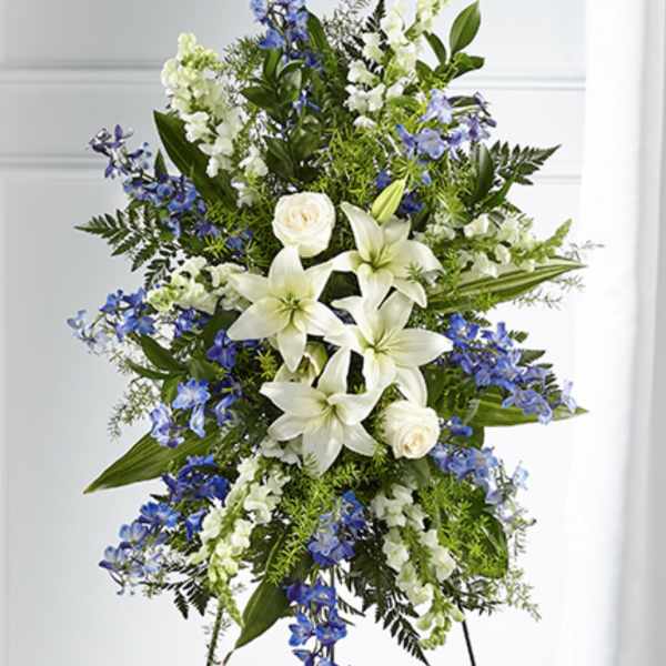 Tall standing spray of white lilies, roses, and blue flowers on a metal easel