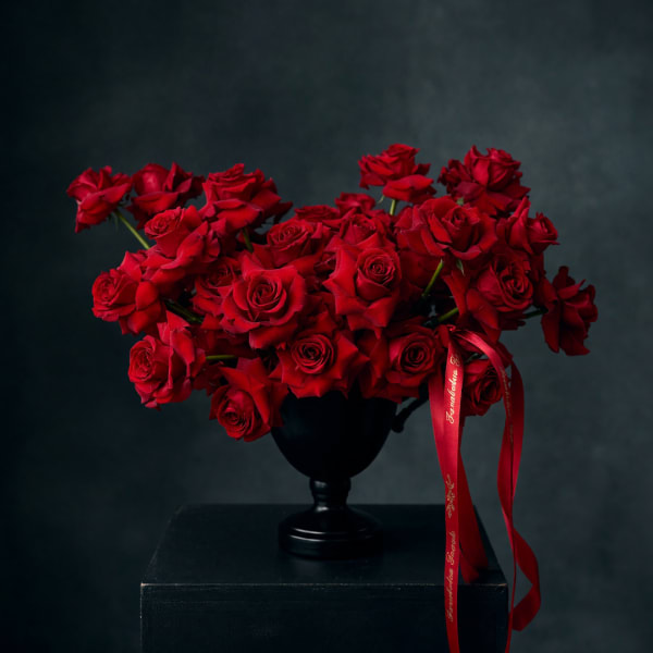 Red roses arranged in a black vase with a red ribbon