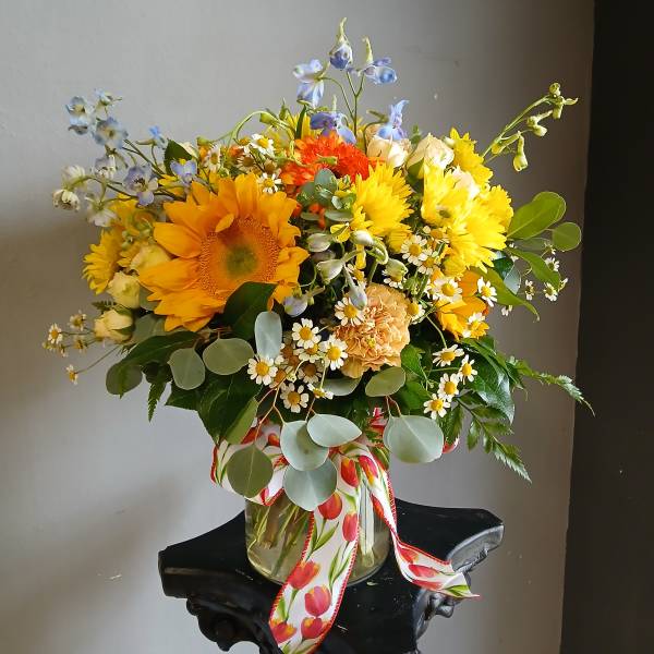 Bright mixed bouquet in a glass vase with sunflowers and daisies