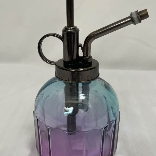 Small blue and purple glass plant mister with dark metal pump and nozzle on a light surface
