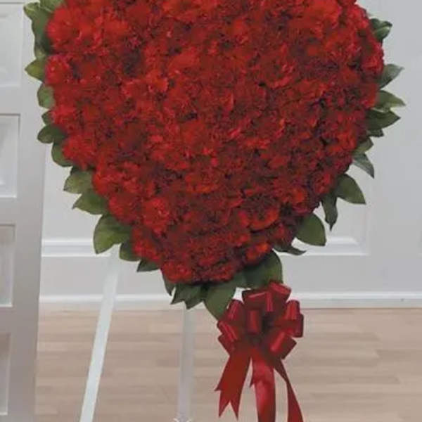 Heart-shaped red floral arrangement on a white stand with a red ribbon