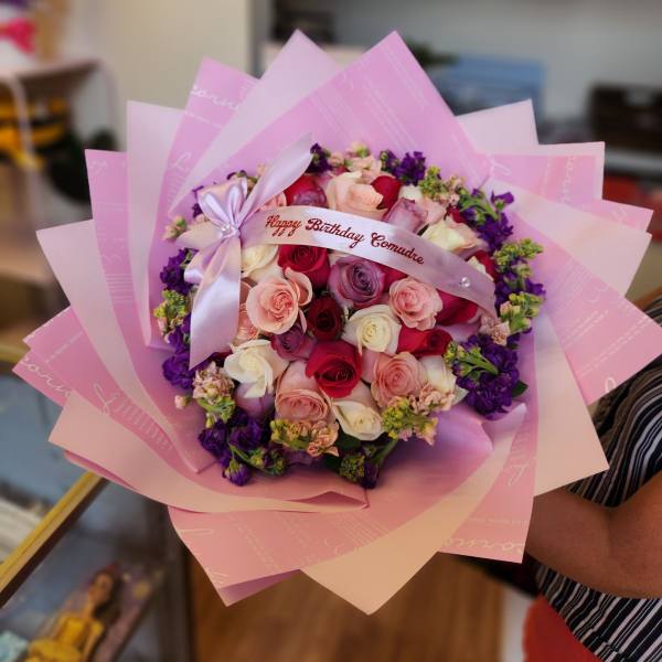 Pink and purple rose bouquet wrapped in pastel paper with a birthday ribbon