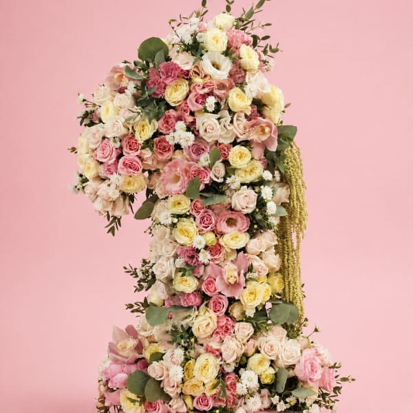 Tall floral arrangement shaped like a number one with pink and cream flowers