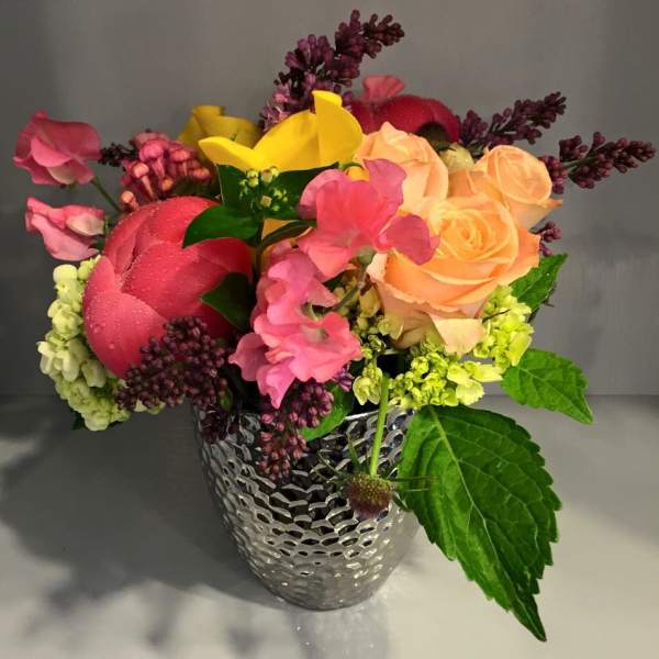 Colorful bouquet of roses, calla lilies, and mixed blooms in a silver vase