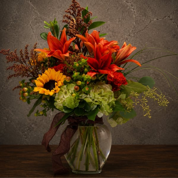 Bright mixed bouquet with orange lilies, sunflowers, and green hydrangeas in a glass vase