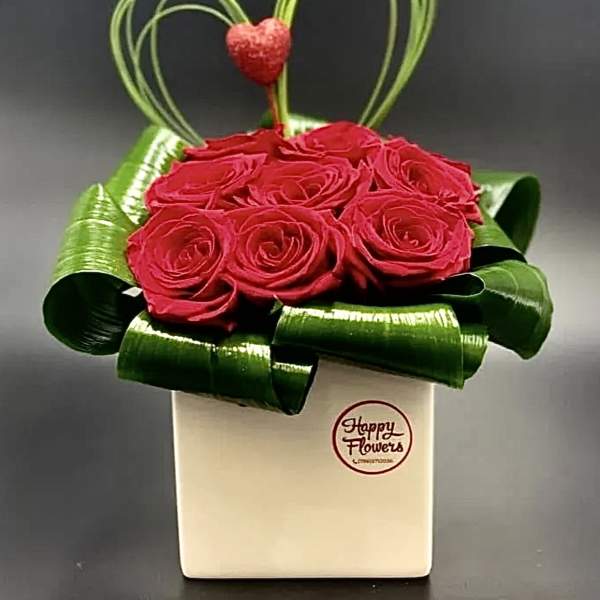 Red roses in a white box with green ribbon loops and a heart topper