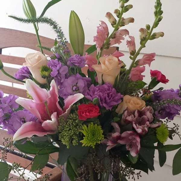 Mixed bouquet of pink, purple, and cream flowers in a clear glass vase