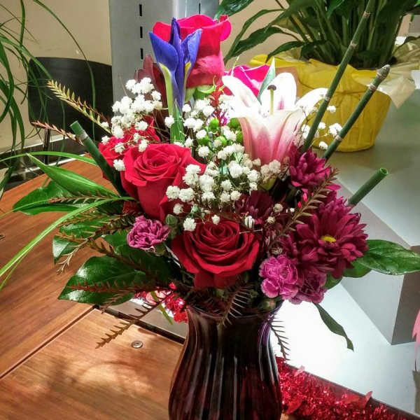 Mixed bouquet of roses, lilies, and daisies in a dark glass vase