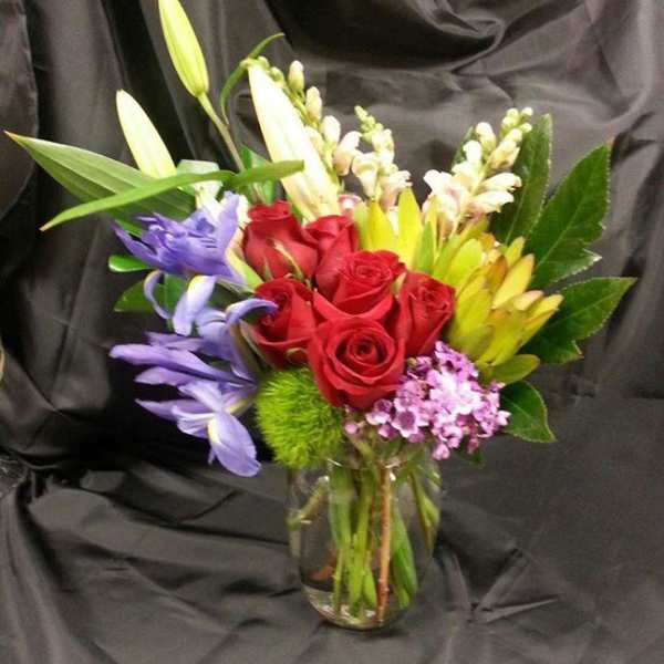 Bouquet of red roses, lilies, and purple flowers in a glass vase