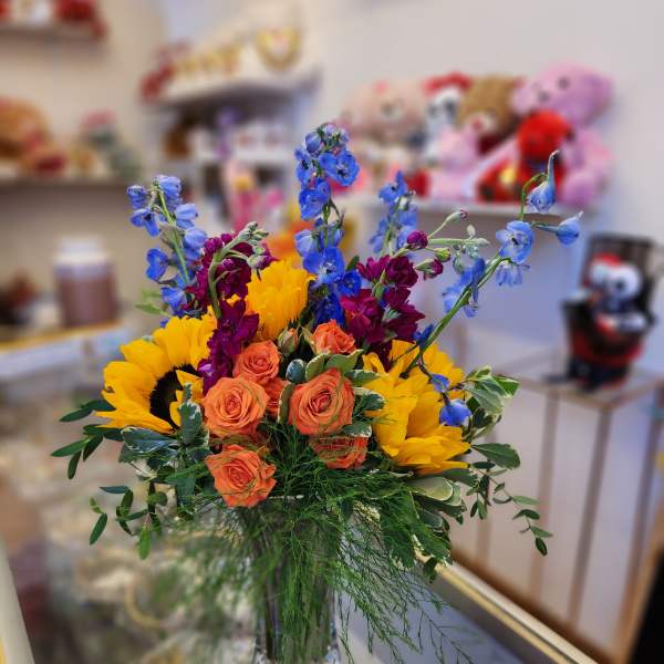 Bouquet of sunflowers, orange roses, and blue delphinium in a glass vase