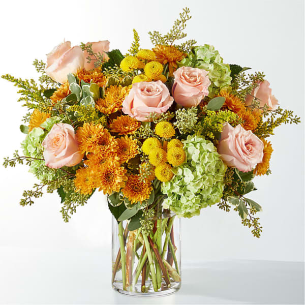 Pink roses, orange mums, and green hydrangeas in a clear glass vase