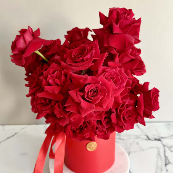 Red roses arranged in a round red box with ribbon