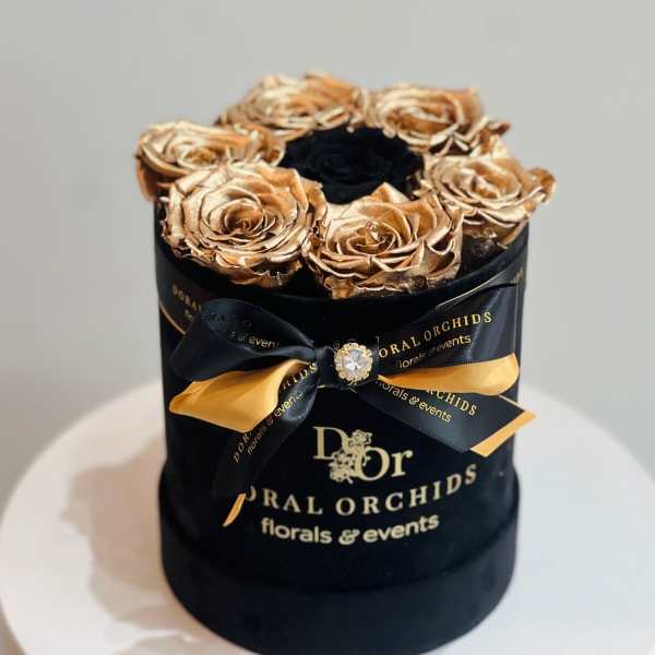 Gold roses in a black round box with a ribbon bow