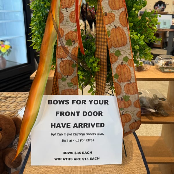 Decorative autumn bows hanging in front of a green wreath with a sign below