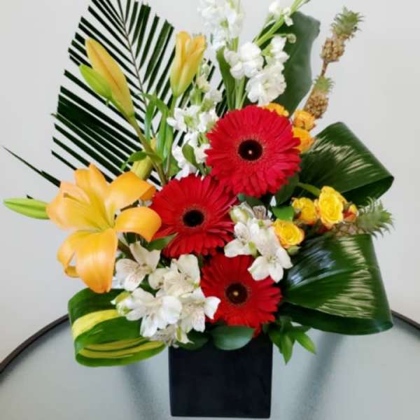 Tropical bouquet with red gerbera daisies, yellow lilies, and white flowers in a black vase
