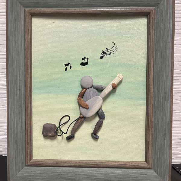 Framed pebble art of a musician playing guitar with musical notes