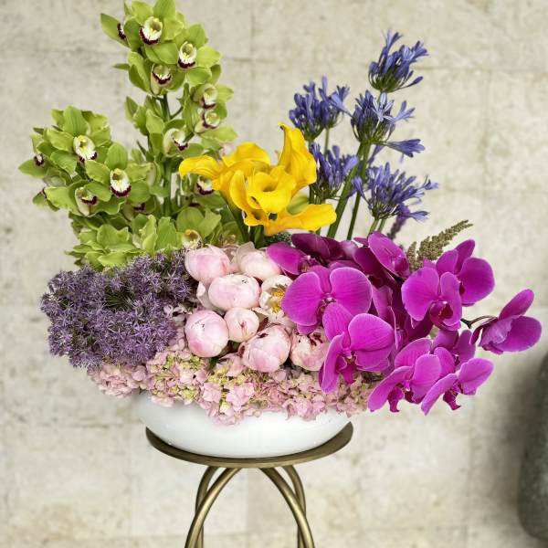 Colorful floral arrangement with orchids, calla lilies, peonies, and hydrangeas in a white bowl