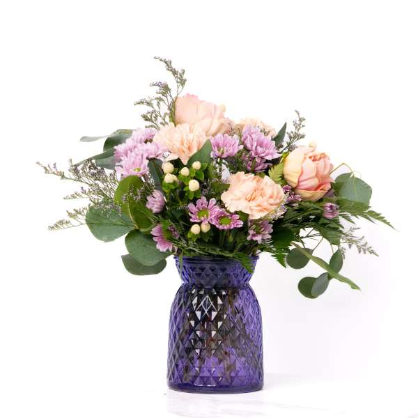 Mixed bouquet of peach roses and carnations with lavender mums in a purple glass vase