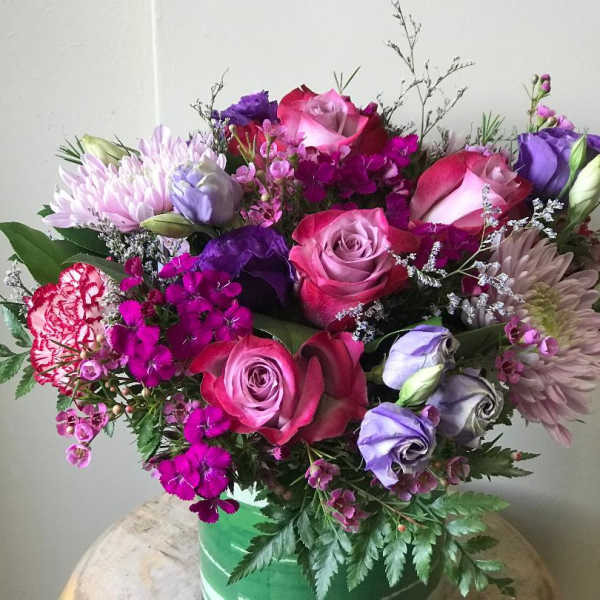 Bouquet of pink and purple roses, chrysanthemums, and carnations in a green vase