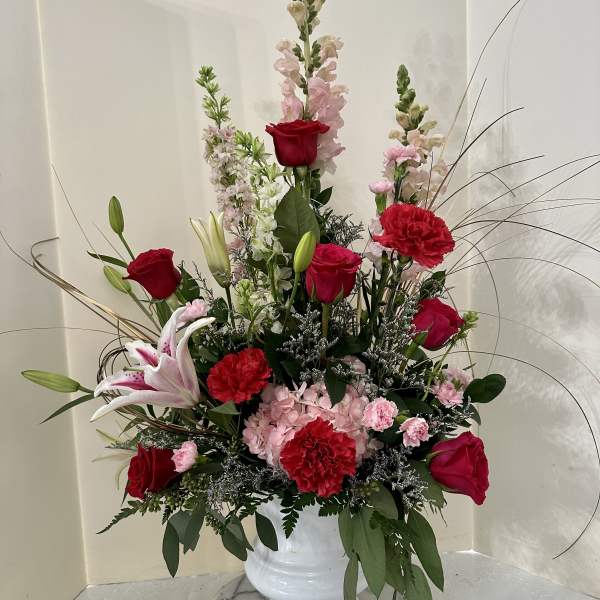 Tall bouquet of red roses, pink lilies, and carnations in a white vase
