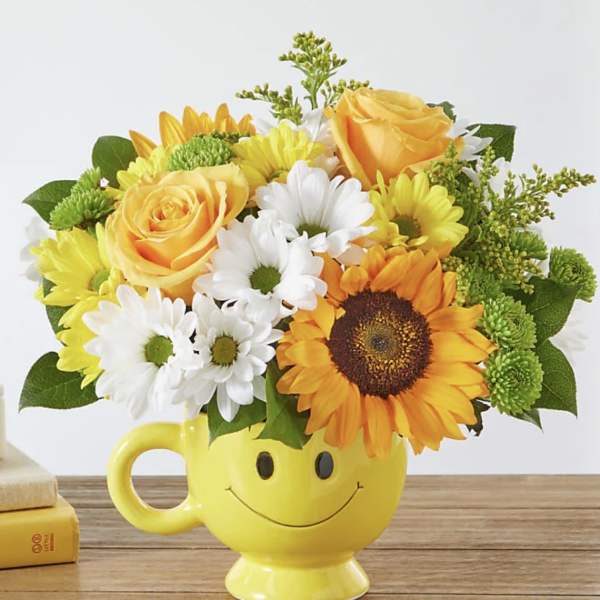 Yellow mug vase with a smiley face holding yellow and white flowers