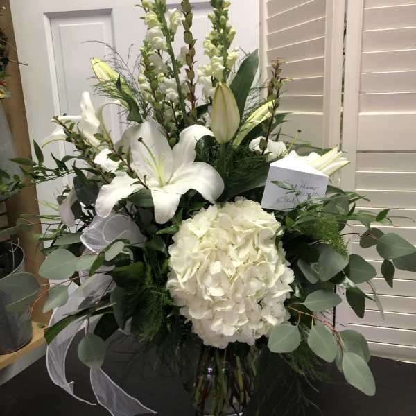 White lilies and hydrangea in a glass vase with greenery