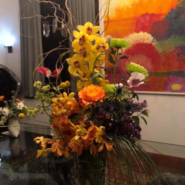 Tall mixed floral arrangement with yellow orchids and orange roses in a glass vase