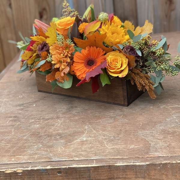 Autumn floral arrangement in a wooden box with orange and yellow blooms