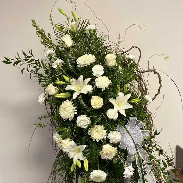 Tall white floral spray with lilies, roses, and ribbon on a twig frame