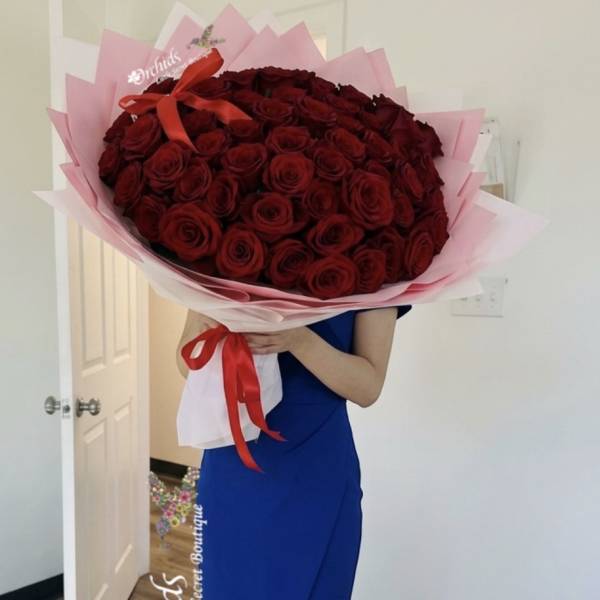 Large bouquet of red roses wrapped in pink paper with a red ribbon