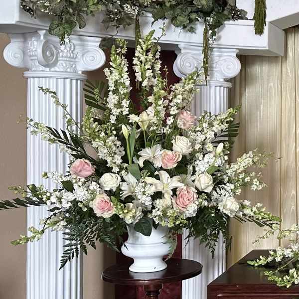 Large arrangement of white lilies and soft pink roses in a white urn