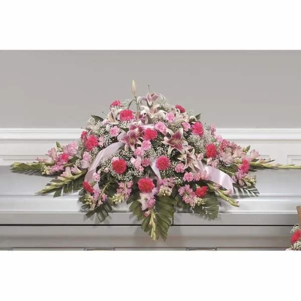 Pink and white floral casket spray with ribbon on a white casket