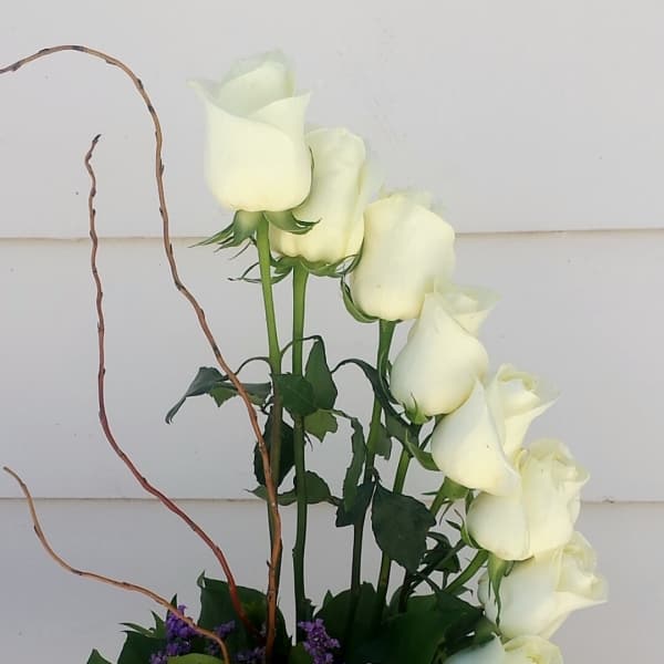 White roses arranged with purple filler in a low vase.