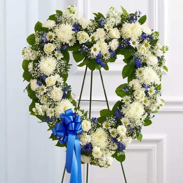 Heart-shaped floral wreath with white and blue flowers on a stand