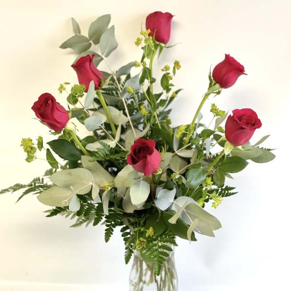 Red roses in a clear glass vase with mixed greenery