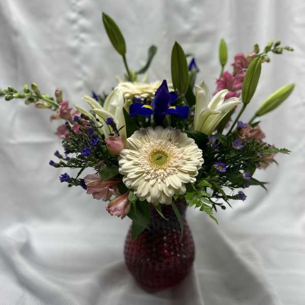 Mixed bouquet with a white gerbera daisy, lilies, and purple accents in a red vase