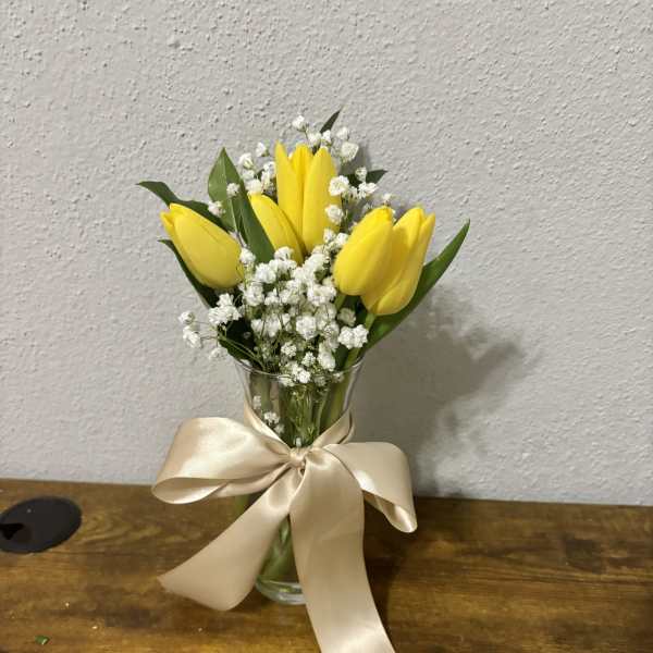 Yellow tulips in a glass vase with white baby's breath and a satin bow