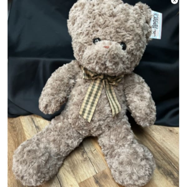 Plush teddy bear with a plaid ribbon bow sitting on a wooden floor
