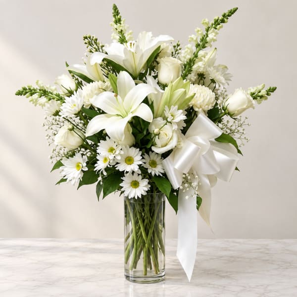 White lilies and daisies arranged in a clear glass vase with a white ribbon