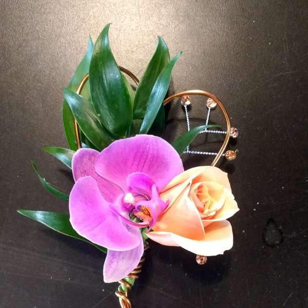 Purple orchid and peach rose boutonniere with green leaves