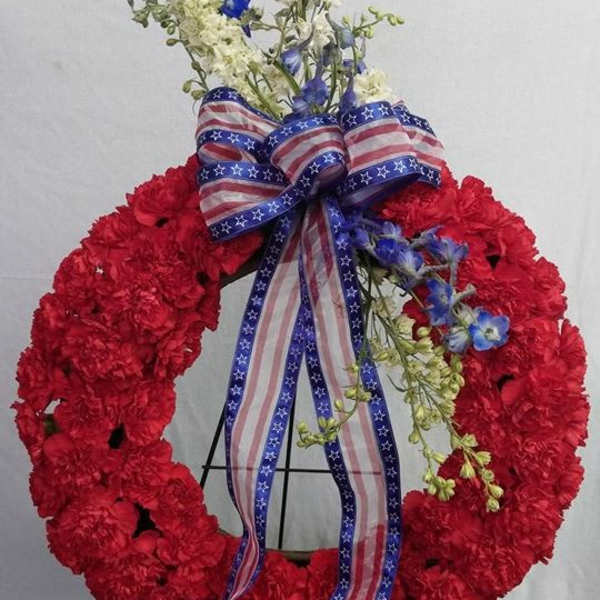 Red floral wreath with blue and white flowers and an American flag ribbon